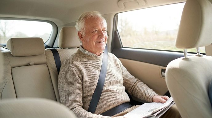 Älterer Fahrgast sitzt angeschnallt auf dem Rücksitz eines Fahrzeugs, Krankenfahrt im Sitzen in München